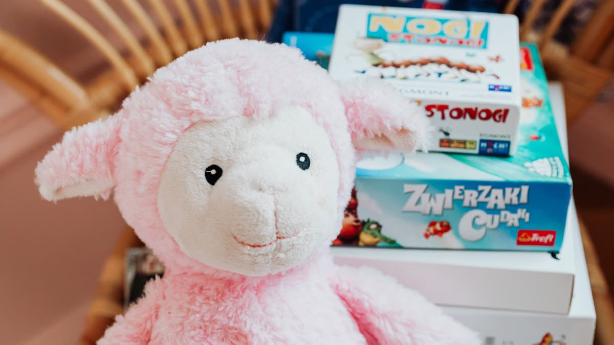 Close-up of a pink plush lamb alongside colorful board games, perfect for children's playrooms.